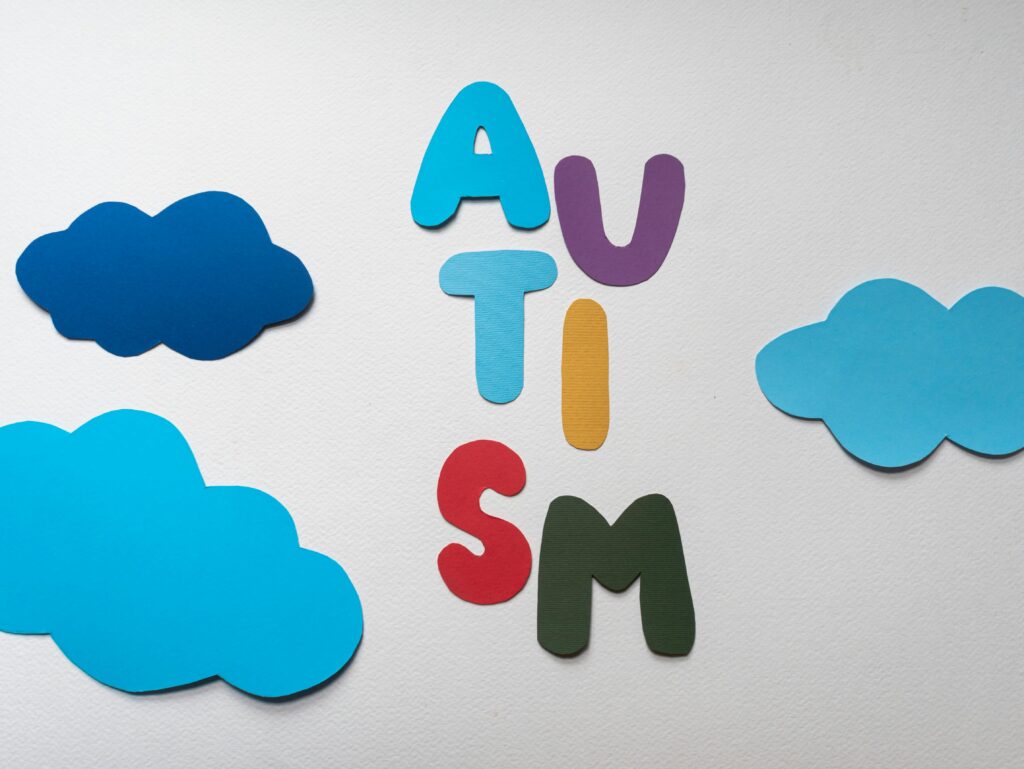 Colorful cut-out letters spelling "AUTISM" with blue paper clouds on a white background.