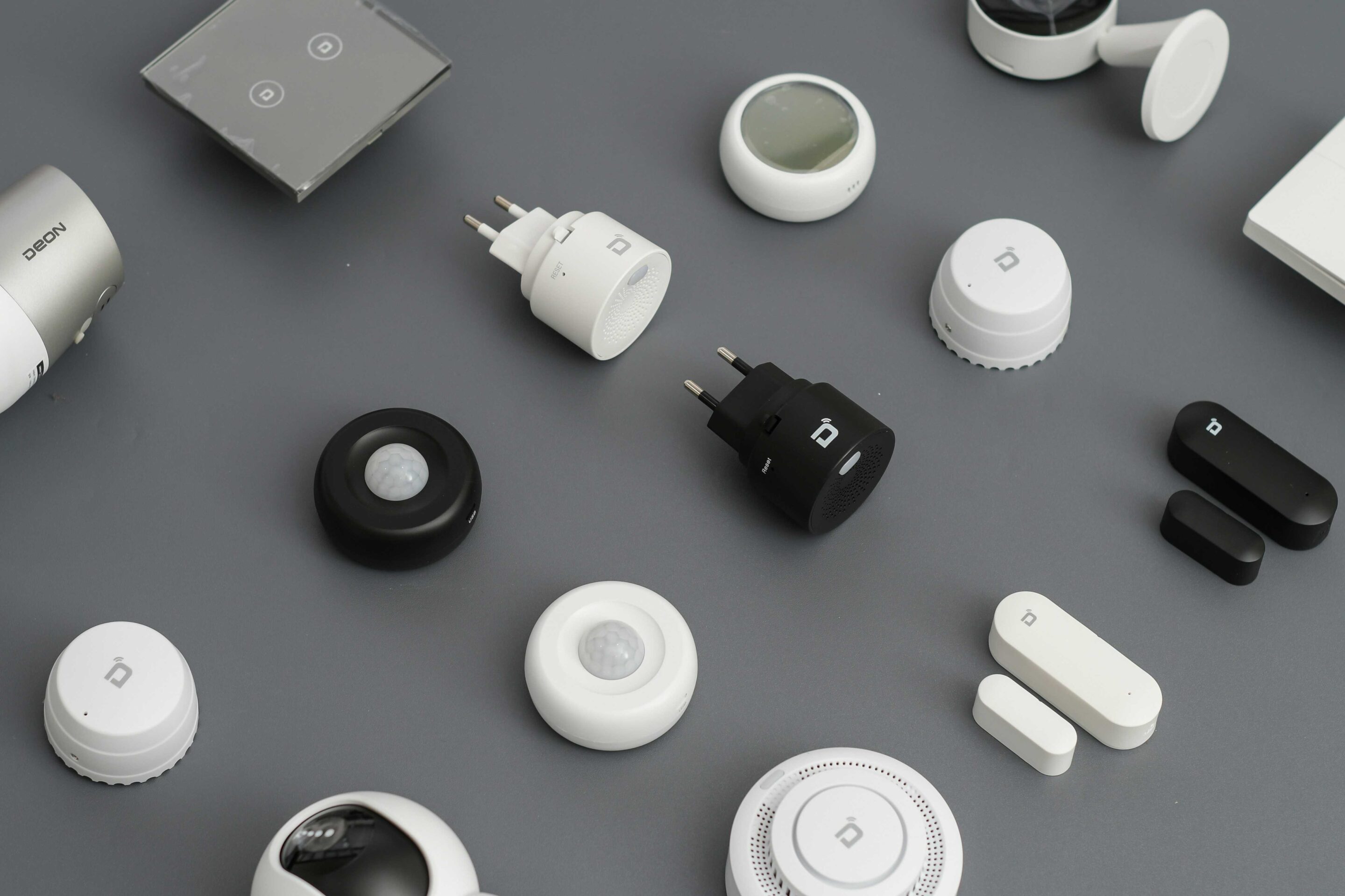 Smart home devices layout featuring motion sensors, smart plugs, switches, and security gadgets on a grey background.